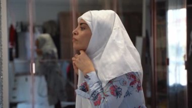 Evde başörtüsü takan orta yaşlı Müslüman kadın portresi başörtüsü takıyor. Aynaya bakıyor. Başörtüsü ile kaplanmış neşeli bir kadın yüzü. Gündelik İslamcı kız.
