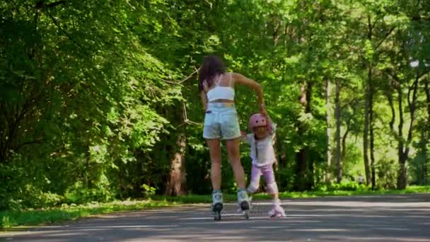 母は夏の晴れた日に公園でローラー付きの小さな娘のインラインスケートを教えています 一緒に幸せな家族の時間 レジャースポーツ活動 — ストック動画