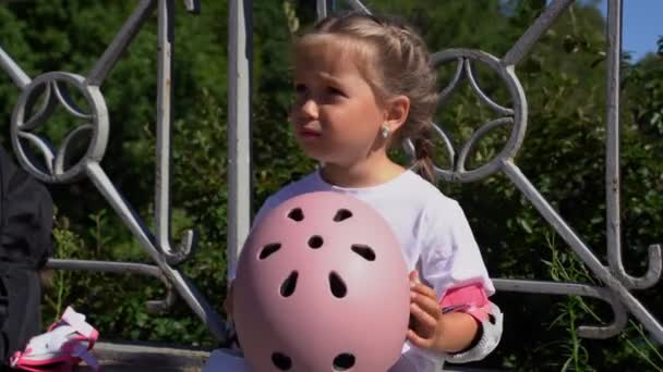 少し不幸な気まぐれな女の子は お母さんが尋ねる何かをすることに同意しない保護ピンクのヘルメットを保持します 母は夏に公園の娘の子供へのインラインスケートローラー保護を置く — ストック動画