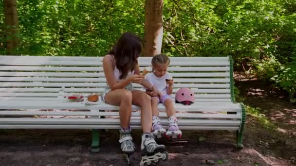 公園でインラインローラーを一緒にスケートした後 母と娘はベンチで軽食を持っています 家族レジャースポーツ活動週末 負のスペースをコピー — ストック動画