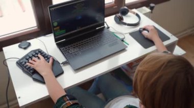 Çocuk el yazısıyla bilgisayar oyunu yazan klavye faresini kapat, çocuk dizüstü bilgisayarla oyun oynuyor. Hobi aktivitesi, çocukların sağlıksız teknoloji bağımlılığı. Yüksek kaliteli 4k görüntü üst görünümü