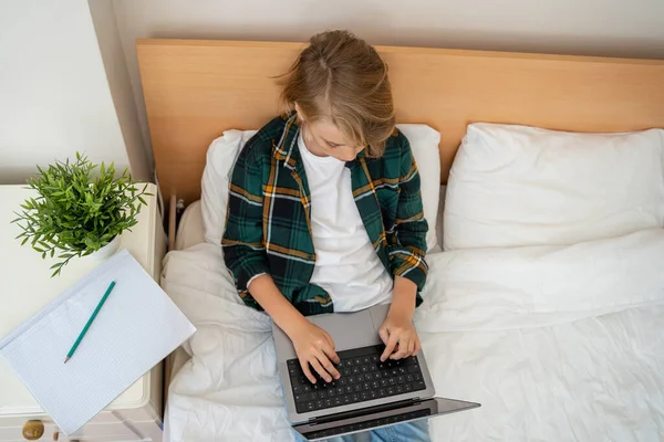 十几岁的男孩使用笔记本电脑 孩子在键盘上打字躺在床上 玩电子游戏 男孩在学习做作业 电子学习 远程教育课高瞻远瞩 — 图库照片
