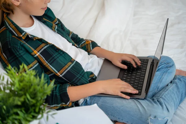 十几岁的男孩使用笔记本电脑 孩子在键盘上打字躺在床上 玩电子游戏 男孩在学习做作业 电子学习 远程教育课 — 图库照片