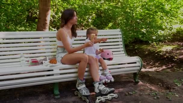 公園でインラインローラーを一緒にスケートした後 母と娘はベンチで軽食を持っています 家族レジャースポーツ活動週末 負のスペースをコピー — ストック動画