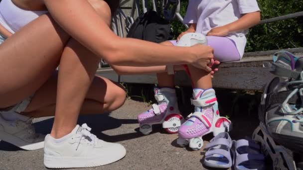 閉鎖お母さんは夏に公園で娘の子供へのインラインスケートローラー膝の保護を置く ファミリーレジャーアウトドアスポーツ活動ゲーム — ストック動画