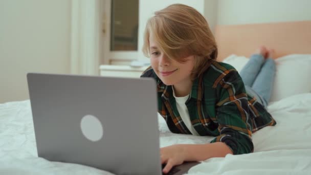 ノートパソコンを使って10代の少年 子供のキーボードのベッドの横に入力します ビデオゲームをプレイする 宿題を勉強している少年 Eラーニング リモートオンライン教育クラス — ストック動画