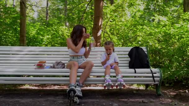 公園でインラインローラーを一緒にスケートした後 母と娘はベンチで軽食を持っています ファミリーレジャースポーツ活動週末 — ストック動画