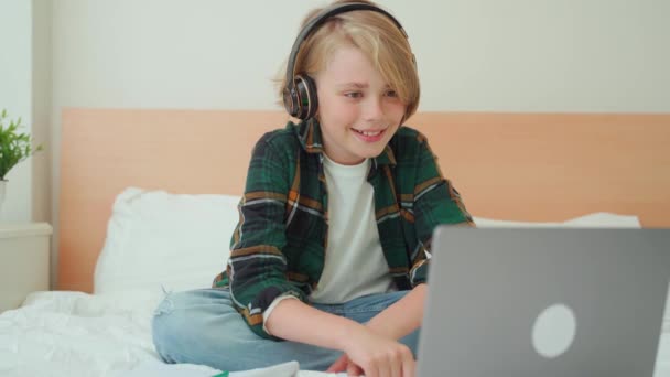 ラップトップとヘッドフォンを使用して10代の子供の少年 ベッドでオンラインビデオコースレッスンを探している子供 チャットビデオ会議宿題を勉強している学校の少年 Eラーニング遠隔教育クラス — ストック動画