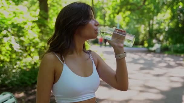 白人の若い女性公園で透明な水のボトルから水を飲む女の子 — ストック動画