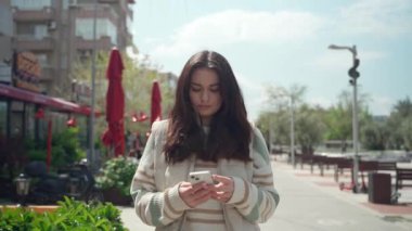 Dışarıda cep telefonuyla yazan mutlu genç bir kadın. Şehirli arka planda akıllı telefon kullanarak yürüyen neşeli genç kız. Sosyal medya, kurye, mafya uygulaması, video izleme, online alışveriş, internette gezinme