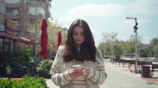 快乐的年轻女子在户外用手机打字 在城市背景下 快乐的少女用智能手机走路 社交媒体 暴民应用程序 观看视频 网上购物 浏览互联网 — 图库视频影像