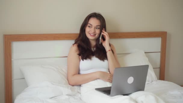 Ung Kvinna Pratar Smartphone När Använder Bärbar Dator Hemma Sängen — Stockvideo