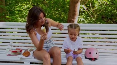 Anne ve kızı halka açık parkta paten kaydıktan sonra bankta atıştırıyorlar. Aile eğlencesi spor etkinliği hafta sonu. 