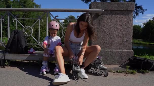 母と小さな娘の女の子は夏の晴れた日に公園でローラーでインラインスケートの準備をします 一緒に幸せな家族の時間 レジャースポーツ活動 — ストック動画