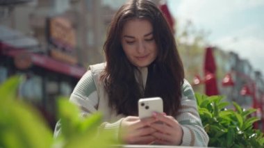Dışarıda cep telefonuyla yazan mutlu genç bir kadın. Şehirli arka planda akıllı telefon kullanan neşeli bir genç kız. Sosyal medya, kurye, mafya uygulaması, video izleme, online alışveriş, internette gezinme