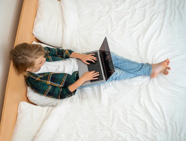 ノートパソコンを使って10代の少年 子供のキーボードのベッドの横に入力します ビデオゲームをプレイする 宿題を勉強している少年 Eラーニング 遠隔教育クラスのトップビュー — ストック写真