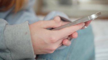 Yan görüş. Evdeki oturma odasında akıllı telefon kullanan ve mesaj yazan bir kız. Genç kadınların yakın plan fotoğrafları.