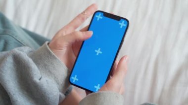 Açık renkli mavi ekranlı akıllı telefon kullanan genç kızın eli video makarasının içeriğini izliyor.