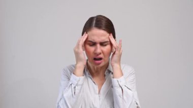 Orta yaşlı bir kadın gri arka plan yüzünden baş ağrısı çekiyor..