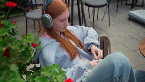 Tiener Meisje Koptelefoon Typen Door Mobiele Telefoon Cafe Buiten Vrolijke — Stockvideo