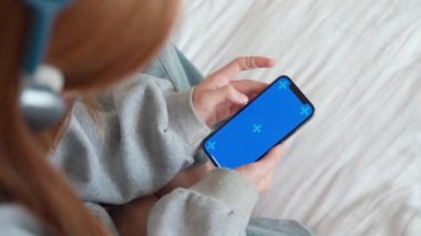 Açık renkli mavi ekranlı akıllı telefon kullanan genç kızın eli video makarasının içeriğini izliyor.