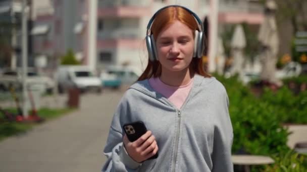 Słuchawki Nastolatek Ruda Dziewczyna Pomocą Smartfona Odkryty Radosna Młoda Kobieta — Wideo stockowe