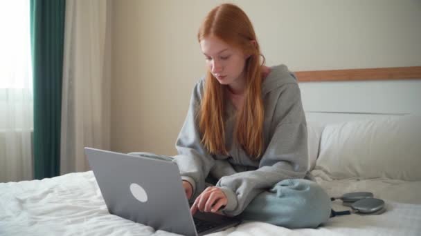 ベッドの上の自宅でラップトップを使用して10代の赤い頭の女の子 若い女性勉強 ガジェットで作業を入力 距離学習 フリーランス 学生セッション オンライン教育 インターネット技術 — ストック動画
