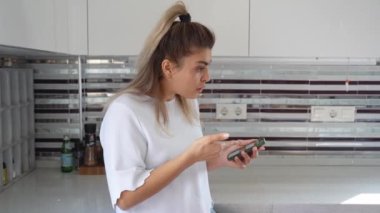 Mutfakta akıllı telefon kullanan bir kadın. İnternetten ev hanımı alışverişi, fatura aramak, internette sörf yapmak, market ya da kafe restoranından yemek siparişi vermek, ev faturasını ödemek.