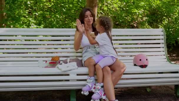 妈妈和女儿一起在公园里滑冰完在线滚轮后 坐在长椅上吃点心 家庭休闲体育活动周末 复制负空间 — 图库视频影像