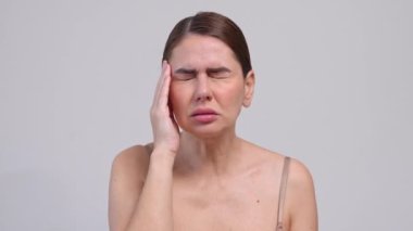 Orta yaşlı bir kadın gri arka plan yüzünden baş ağrısı çekiyor..