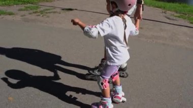 Anne ve küçük kız yaz güneşli bir günde halka açık parkta paten kaymaktan hoşlanırlar. Mutlu aile zamanları, spor aktiviteleri..