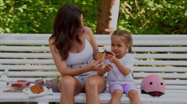 Anne ve kızı halka açık parkta paten kaydıktan sonra bankta atıştırıyorlar. Aile eğlencesi spor aktivitesi hafta sonu. Negatif alanı kopyala