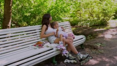 Anne ve kızı halka açık parkta paten kaydıktan sonra bankta atıştırıyorlar. Aile eğlencesi spor aktivitesi hafta sonu. Negatif alanı kopyala