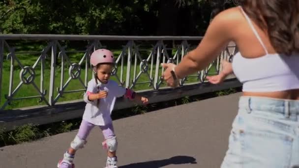 母は夏の晴れた日に公園でローラー付きの小さな娘のインラインスケートを教えています 一緒に幸せな家族の時間 レジャースポーツ活動 — ストック動画