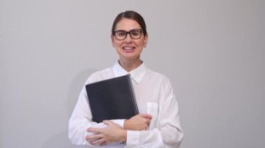 Gözlüklü orta yaşlı kadın, gri arkaplanda siyah klasörlü pozlar veriyor. Kendine güvenen Kurumsal Zarif. Boşluğu, Boşluğu, Şablonu Kopyala