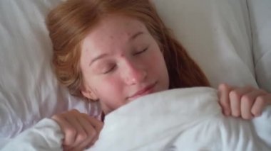 Yatağında Battaniyeyle Yatan Güzel Genç Kadın 'ın yakın çekimi. Kız 'ın en iyi görüntüsü Utangaç ve Battaniyeli Yüzünün Örtüsü. Kadın Gülümseyen ve Kameraya Bakan. Sağlıklı Sabah Rutini