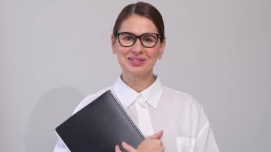 Gözlüklü orta yaşlı kadın, gri arkaplanda siyah klasörlü pozlar veriyor. Kendine güvenen Kurumsal Zarif. Boşluğu, Boşluğu, Şablonu Kopyala