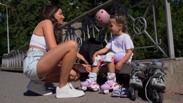 母は夏に公園で娘の子供へのインラインスケートローラー膝の保護を置く ファミリーレジャーアウトドアスポーツ活動ゲーム — ストック動画
