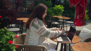 Kafede dizüstü bilgisayar kullanan genç bir kız kahve içiyor. Neşeli genç bir kadın oturmuş online öğrenci makalesini izliyor, sınav çalışmasını çiçek arka planında yapıyor.