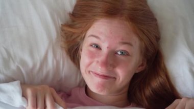 Yatağında Battaniyeyle Yatan Güzel Genç Kadın 'ın yakın çekimi. Kız 'ın en iyi görüntüsü Utangaç ve Battaniyeli Yüzünün Örtüsü. Kadın Gülümseyen ve Kameraya Bakan. Sağlıklı Sabah Rutini