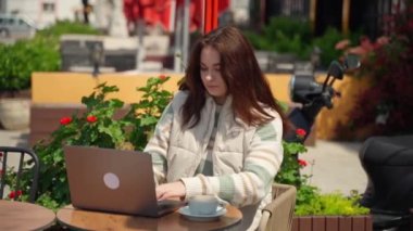 Kafede dizüstü bilgisayar kullanan genç bir kız kahve içiyor. Neşeli genç bir kadın oturmuş online öğrenci makalesini izliyor, sınav çalışmasını çiçek arka planında yapıyor.
