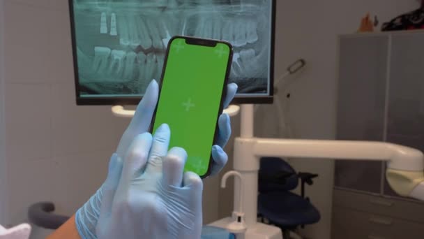 牙科医生手消毒手套在牙科诊所的监视器上有绿色屏幕手机 牙齿矫正专家滚动智能手机彩色键屏模型模板展示牙齿 — 图库视频影像