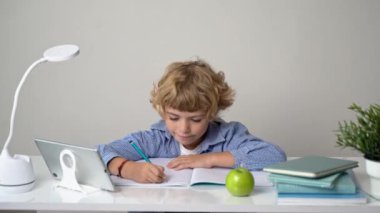 İlkokul öğrencisi erkek ya da kız, mektup yazıyor, masa başında okuyor. Beyaz arka planda okula geri döndüm. İlk ders, alfabe, öğrenci bilgisi. Reklam için boşluk kopyala.