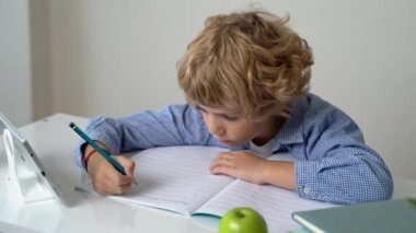 İlkokul öğrencisi erkek ya da kız, mektup yazıyor, masa başında okuyor. Beyaz arka planda okula geri döndüm. İlk ders, alfabe, öğrenci bilgisi. Reklam için boşluk kopyala.