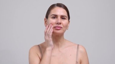 Orta Yaşlı Kadın Yüze Dokunan Beyaz Arkaplan. 40 yaşındaki kadın kameraya bakıp gülümsüyor. Doğal güzelliğinin, kendine olan saygısının ve sağlığının tadını çıkarma kavramı. Doğal Kozmetik Cilt