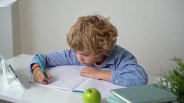 İlkokul öğrencisi erkek ya da kız, mektup yazıyor, masa başında okuyor. Beyaz arka planda okula geri döndüm. İlk ders, alfabe, öğrenci bilgisi. Reklam için boşluk kopyala.