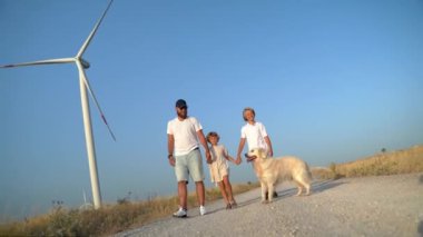 Mutlu aile babası çocuklar Golden Retriever köpek kızı kırsal yolda yel değirmeni rüzgar jeneratörüyle yürüyor. Özgürlük, çocukluk, çevre dostu enerji gücü.