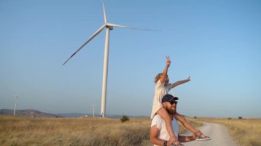 Omzunda Çocuğunu Taşıyan ve Rüzgar Tarlasında Yürüyen Adam. Mutlu Baba ve Kız Daha Çevresel, Sürdürülebilir Enerjide Birlikte Temiz Hava ve Zamanın Tadını Çıkarıyorlar