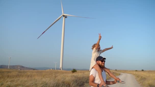 男人把他的女儿抱在肩上 走在风车场 快乐的父亲和女儿在一起享受时光 在更环保 可持续 高效的能源中呼吸洁净的空气 — 图库视频影像