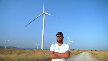 Rüzgâr jeneratörüyle kırsal yolda göğsün üzerinde duran mutlu, kendine güvenen bir adam. Özgürlük, Çevre dostu enerji gücü. sürdürülebilir tüketim